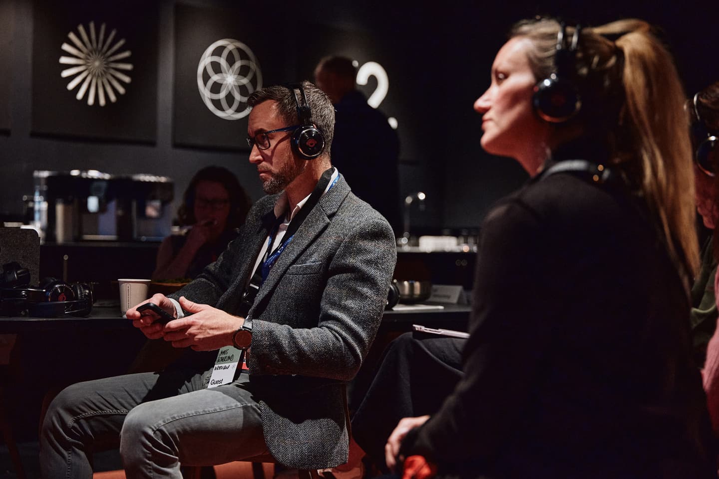 Several people wearing headphones sit and listen attentively in a dimly lit room with abstract art on the walls.
